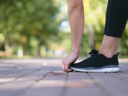 Feet in sports shoes and hands of woman who doing standing crease on the paved path in public park...