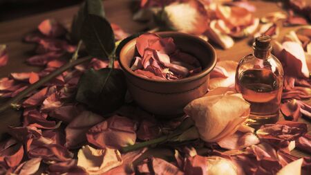 Clay bowl and aroma oil glass bottle among roses petals on the wooden table, natural raw material, selected focus.の写真素材