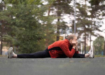 Blond attractive caucasian woman doing middle split stretching on the sports area outdoor in summer,...