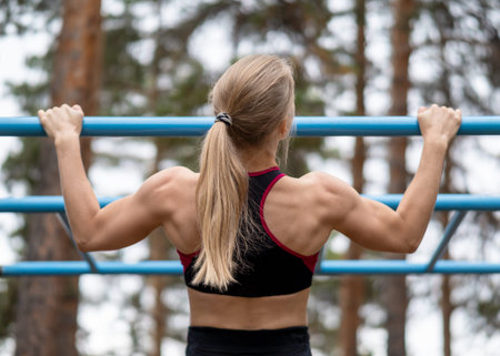 Athletic blond beautiful caucasian woman doing chin ups exercise on the sports ground outdoor in...