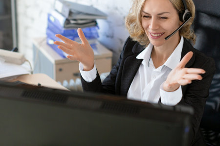 Distance business. Adult caucasian woman in formalwear with headset sits at the computer in the...