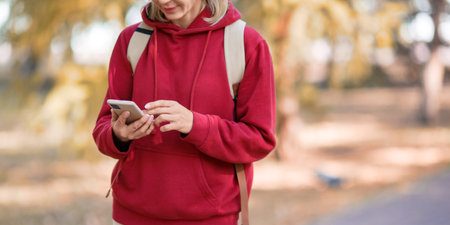 Digital addiction. Hands with mobile of walking person in the park outdoor in autumn, close up,...