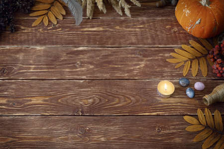 Autumn authentic layout on wooden backdrop with dry leaves, pumpkin, ashberry, agate gemstones, bottle, candle and feather, copy space, selective focus.の写真素材
