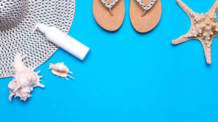 Summer beach vacation flatlay. Sunhat, seashells, female sandals, lotion and starfish on blue background, copy space.の写真素材