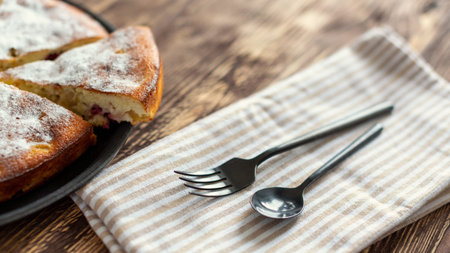 Homemade food. A plate with sliced apple pie, black fork, teaspoon and striped kitchen linen napkin...