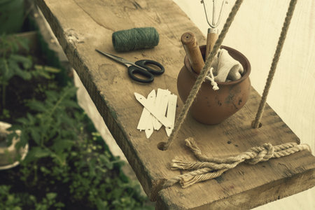 Home female garden, vintage style. Small cute garden stuff and a clay pot lie on a hanging rough wooden shelf in greenhouse, selective focus.の写真素材