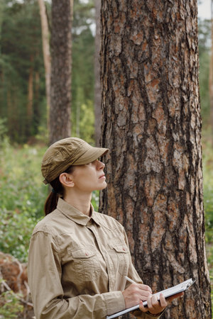 A woman park ranger in uniform with a clipboard control the forest area in summer, vertical photo,...