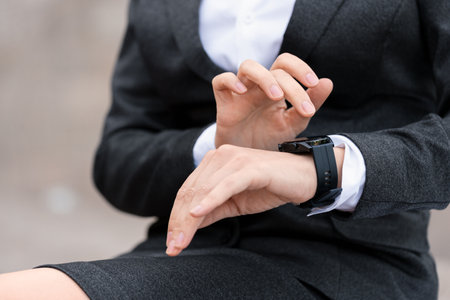 Female hands using smartwatch, close-up. Faceless woman in formal wear sits outdoor in the city, selective focus.の写真素材