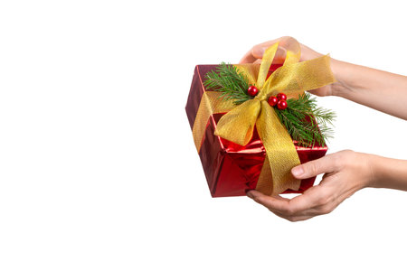 Female hand with shiny red Christmas gift box decorated with a golden bow and fir twigs, close up,...