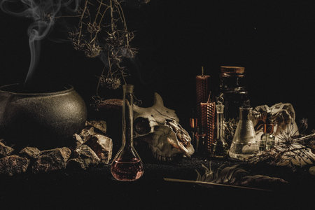 Witchcraft or alchemistry altar. Goats skull, flasks, dry herbs, iron cauldron, wax candles, smoking...
