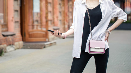 Faceless slim woman in stylish outfit at city steet using her mobile, selected focus.