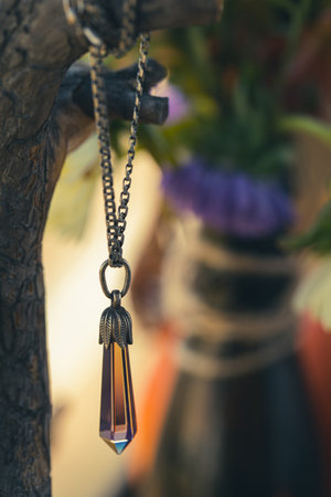 Magic pendant with an amethyst crystal on an atmospheric natural background, vertical format, selective focus. Mojo, amulet, handmade, jewelry concept.の写真素材