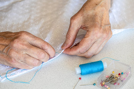 Elderly female hands in the process of hand sewing, close-up, selective focus. Lifestyle, hobby,...