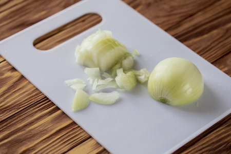 Half-chopped onion head lies on a white cutting board on a wooden table, selective focus.の写真素材