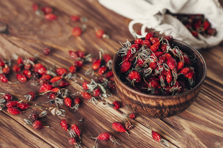 Rosehip fruits in a clay bowl and scattered nearby on a wooden surface, selective focus. Food, medicinal herbs, recipes, traditional medicine, natural ingredients, autumn, harvest concept.の写真素材