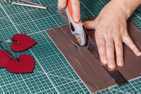 Tanners hands cut leather using work tool on a green cutting mat, close-up, process.
