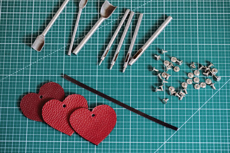 Tanners green cutting mat with work tools and red leathers hearts, close-up, selective focus....