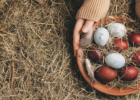 Female hands with clay plate of Easter painted eggs among hay background, close-up, copy space. Atmospheric, Ostara, March, spring, religion, culture, symbol, holiday, paganism, home altar concept.の写真素材