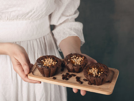 Female hands in vintage white dress hold a small wooden tray with freshly baked muffins and coffee beans, copy space. Atmospheric, cooking, baking, homemade food, pastryの写真素材