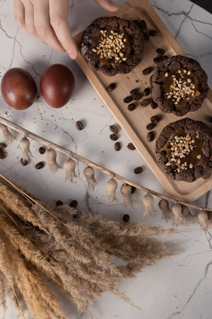 Female fingers take a muffin from small wooden tray next to eggs, coffee beans and decorative dry...