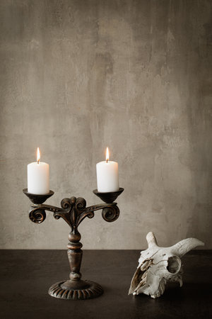 Beautiful vintage metal candelabrum with two burning candles and goats skull on the table, vertical image, copy space.の写真素材