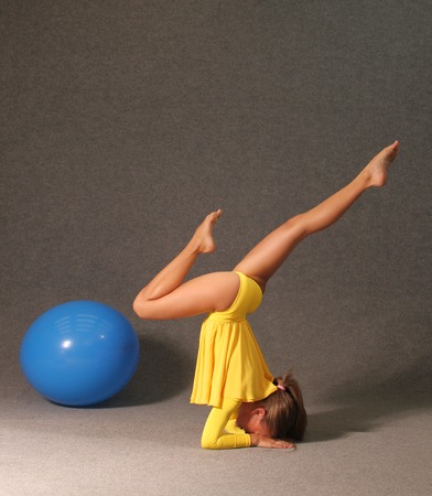 A girl in a yellow dress in the gym is engaged in gymnastics, a blue ball lies beside her.の写真素材