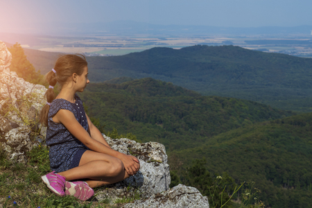 The girl sits on the mountain and looks into the distance.の写真素材