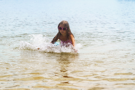 Happy little girl playing in shallow water wavesの写真素材