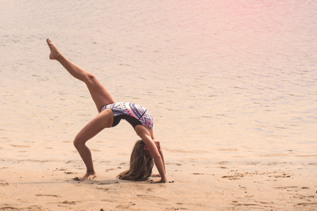 schoolgirl making gymnastics on seashoreの写真素材