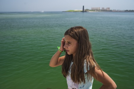 Summer sunny day.The girl sits on the shore of the ocean, a stone beach, water of green color.の写真素材