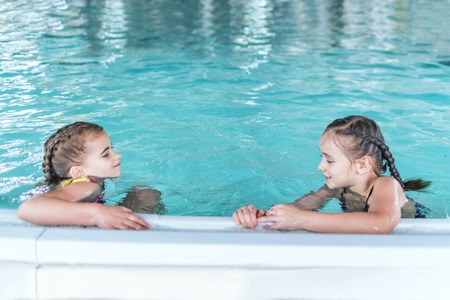 Two little girls having fun in the pool.Two little girls swim in the pool. Two friends in the pool.の写真素材