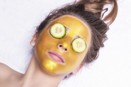 Beautiful girl with a cosmetic mask on the face of golden color. Beautiful model removing golden facial skin cosmetic. Beauty skincare .Close-up. Free space. Woman gold mask. .の写真素材