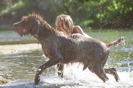 Little girl playing in the river with a dog on a summer sunny day.The concept of playing with a dog in nature and walking on the beach with Pets.Little girl playing with dog.の写真素材