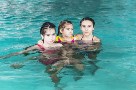 Three sisters in the pool. Three happy girls play in the pool.Beautiful girls swim and having fun in water.Active holiday.Three girls swim in the pool.の写真素材