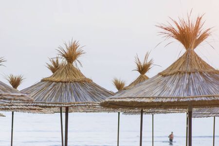 Sun beds with a thatched roof on the seashore.Sun umbrellas and beach beds on the sea coastの写真素材