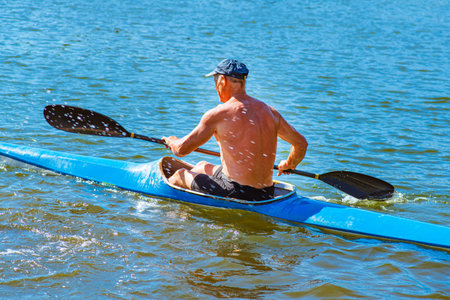 A man swims in a canoe on the river. A man in a boat on a sunny summer day. Blue and yellow boat.Man...