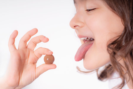 Cheerful girl plays and eats chocolate round sweets on a light background,world chocolate...