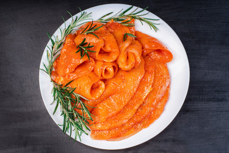 Sottilissime in red marinade on a white kitchen plate with a branch of razmarin and spices on a...