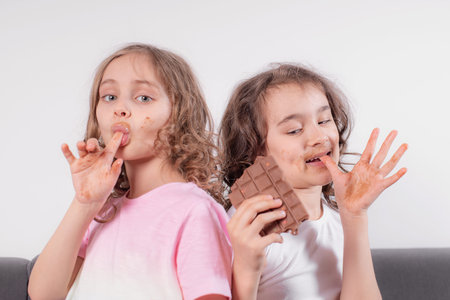Children and chocolate.Two cheerful girls eat chocolate on a light background.