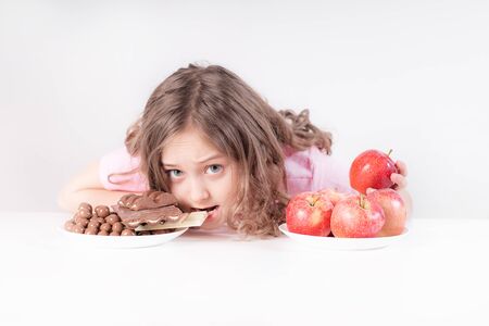 Children and chocolate. A cheerful girl chooses between chocolate and apples. But the choice is for chocolate.Healthy eatingの写真素材