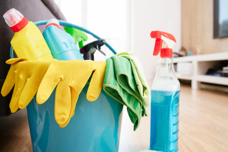 Blue bucket for cleaning with yellow gloves and a variety of detergents with rags. Room...