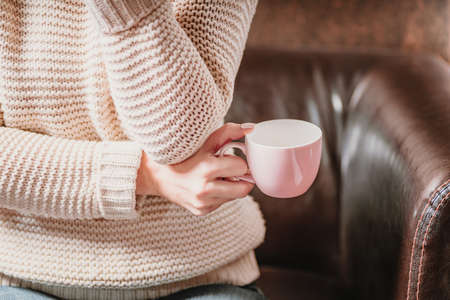 Close-up.Girl in a beige sweater holds a pink cup of tea in her handsの写真素材