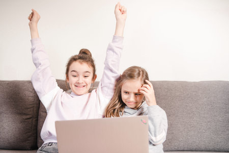 One girl is glad to another sad looking at the computer.Two girls are engaged in distance learning....