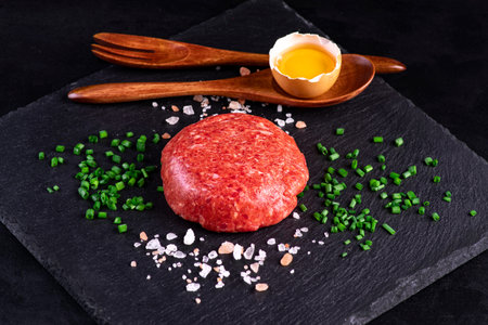 Tartare on a black ceramic board with green onions, egg yolk and salt.の写真素材