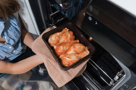 Pickled chicken drumstick for the oven.Female hands put chicken meat in the oven for cooking.の写真素材