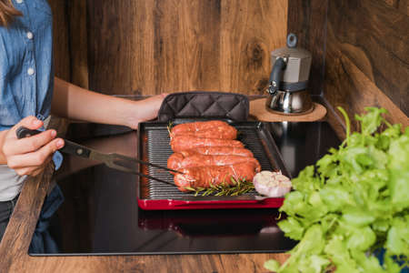 Grilled sausages.Girl prepares grilled sausages in a frying pan in the kitchen.の写真素材