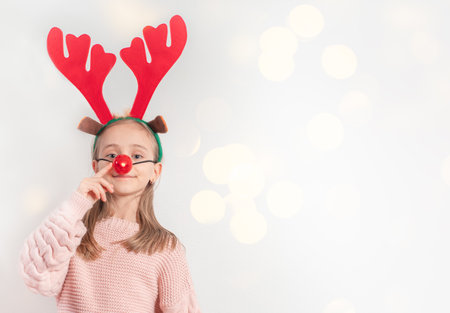 Santa Claus helper concept. Close-up photo portrait of a cheerful adorable positive girl fashionable mask on her head made of funny Christmas deer antlers on a white background. Good New Year spirit. Copy space.の写真素材
