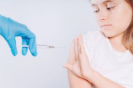 Girl does not want to be vaccinated.Girl with stop vaccination gesture against blue background.Protest sign.Vaccination.Anti vaccination against coronavirus.Girl shows hand to doctor and refuses vaccination againstの写真素材