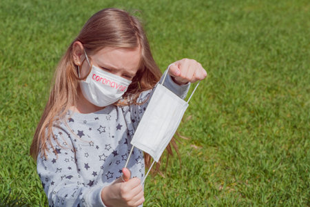 Little girl plays in nature with a mask from viruses on her face. Coronavirus and children. Sad child. Masks from coronavirus.の写真素材