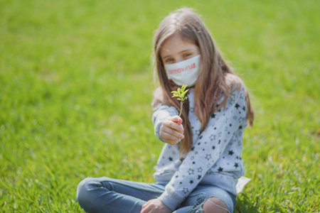 Flu epidemic, self-isolation and coronavirus protection concept.A little girl in a protective mask on her face is resting on the green grass in nature.の写真素材